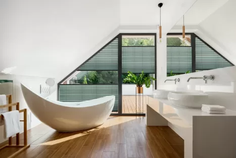 Elegant attic bathroom with stylish bathtub, wooden floor and balcony door